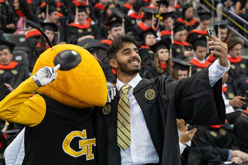 Graduation photo, student taking a selfie with Georgia Tech mascot, Buzz.